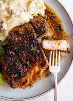 Pan fried pork chop with bite on a fork served on a plate with mashed potatoes.