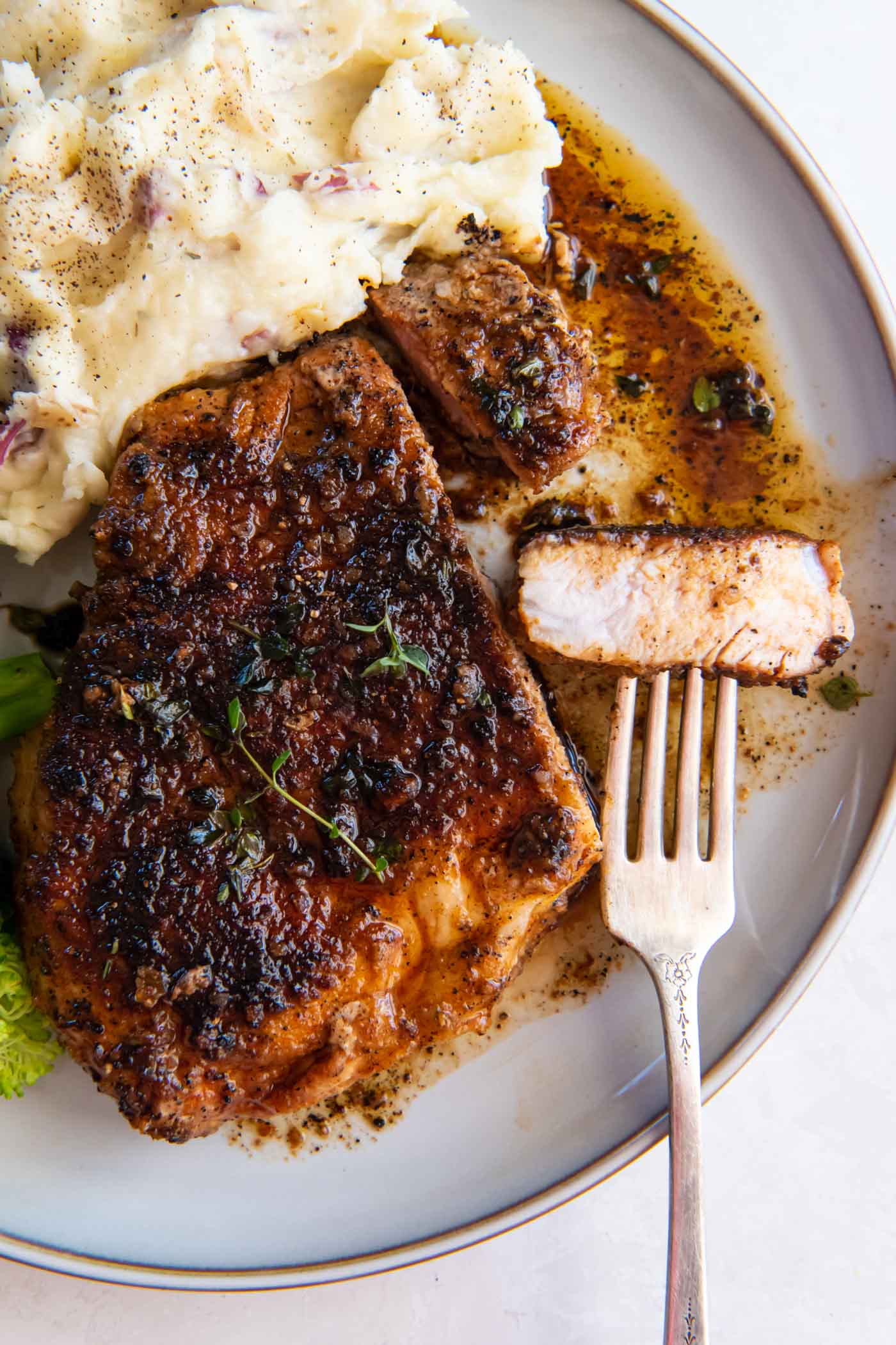 Pan fried pork chop with bite on a fork served on a plate with mashed potatoes.