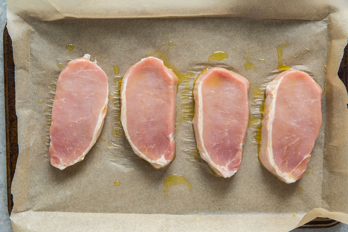 preparing uncooked pork chops with olive oil on baking sheet