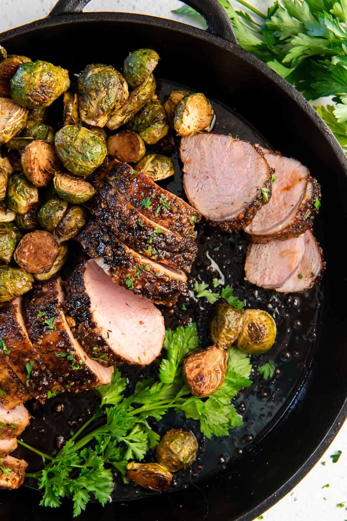 baked pork tenderloin sliced in a cast iron skillet with brussels sprouts