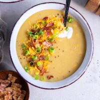 Bowl of potato soup topped with sour cream, shredded cheddar, bacon and green onions.