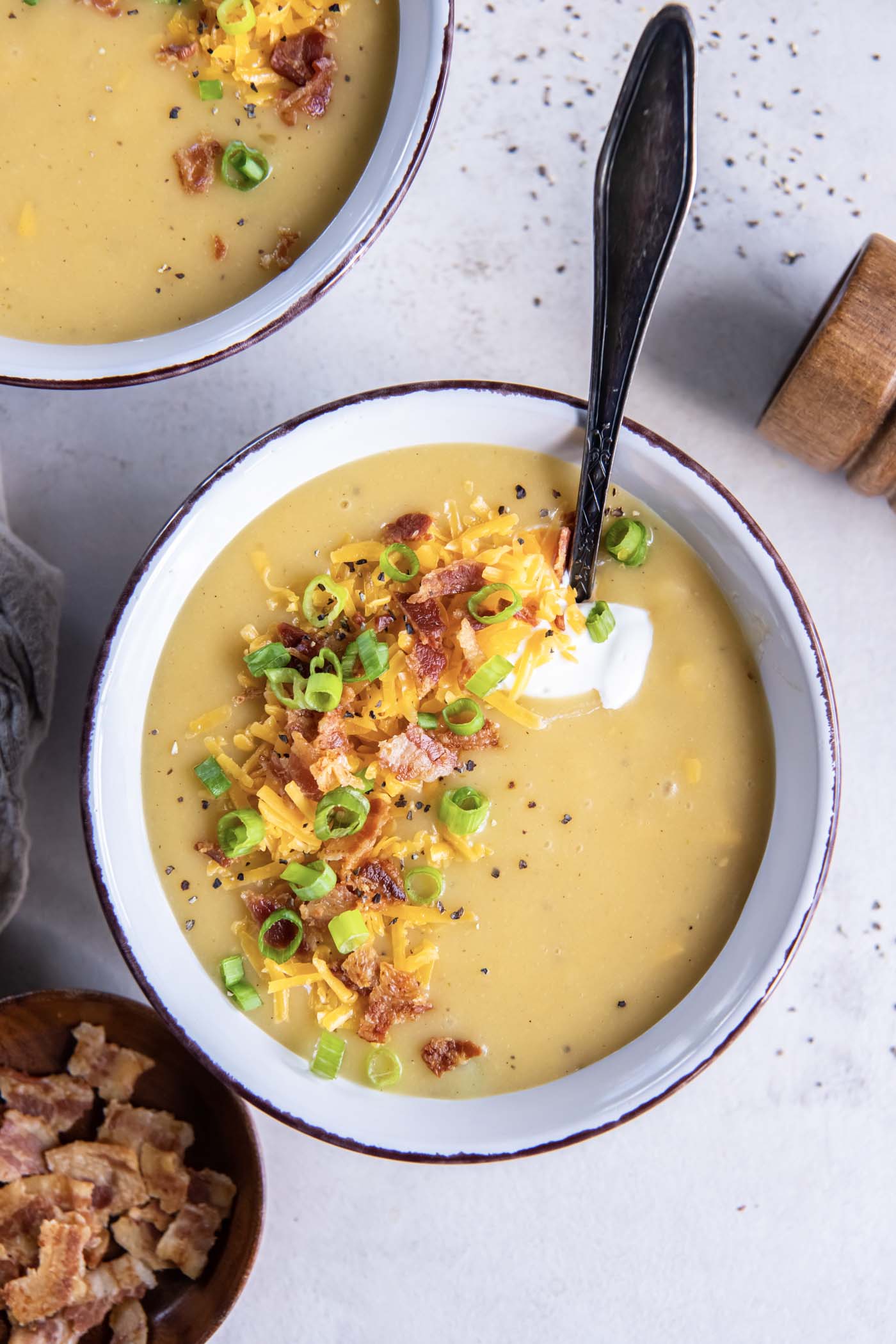 Bowl of potato soup topped with sour cream, shredded cheddar, bacon and green onions.