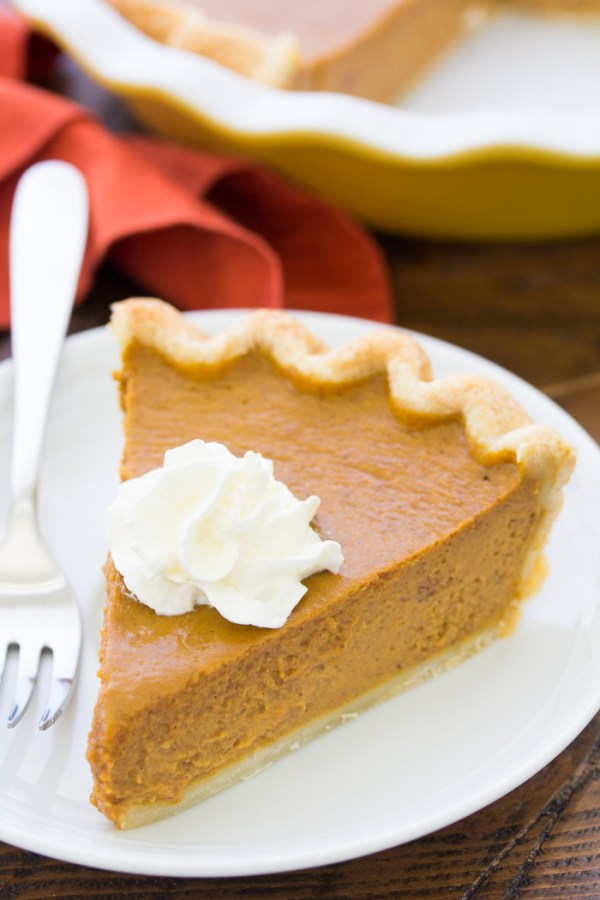Side view of a slice of pumpkin pie served with whipped cream.