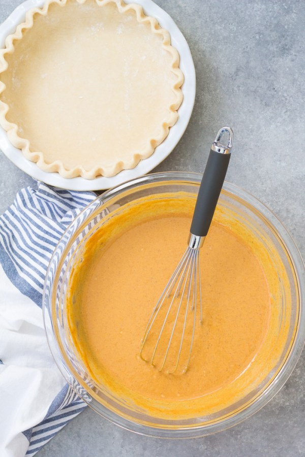 Pumpkin pie filling in a large bowl with a whisk and an unbaked homemade pie crust.
