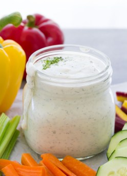 Side view of ranch dressing in a jar, surrounded by veggies.