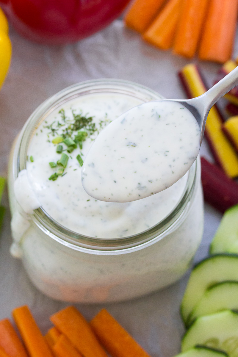 Ranch dressing on a spoon held over jar of dressing.