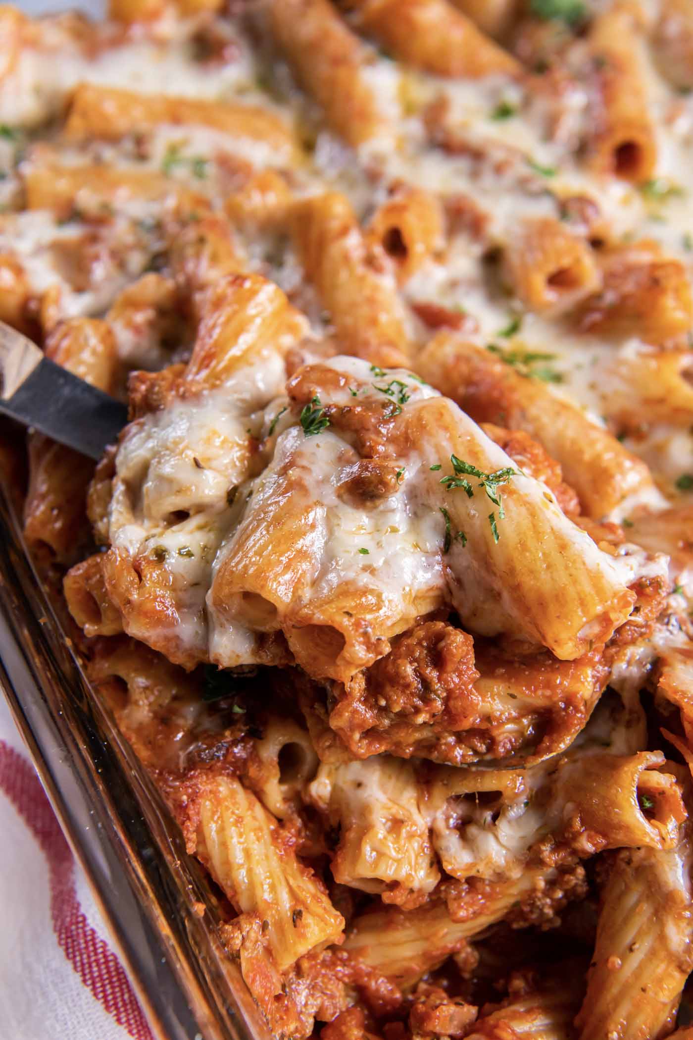 Close up of baked rigatoni pasta on a serving spoon set in baking dish.