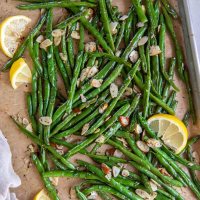 Roasted green beans with sliced almonds and lemon wedges on a baking sheet.
