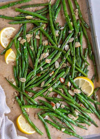 Roasted green beans with sliced almonds and lemon wedges on a baking sheet.