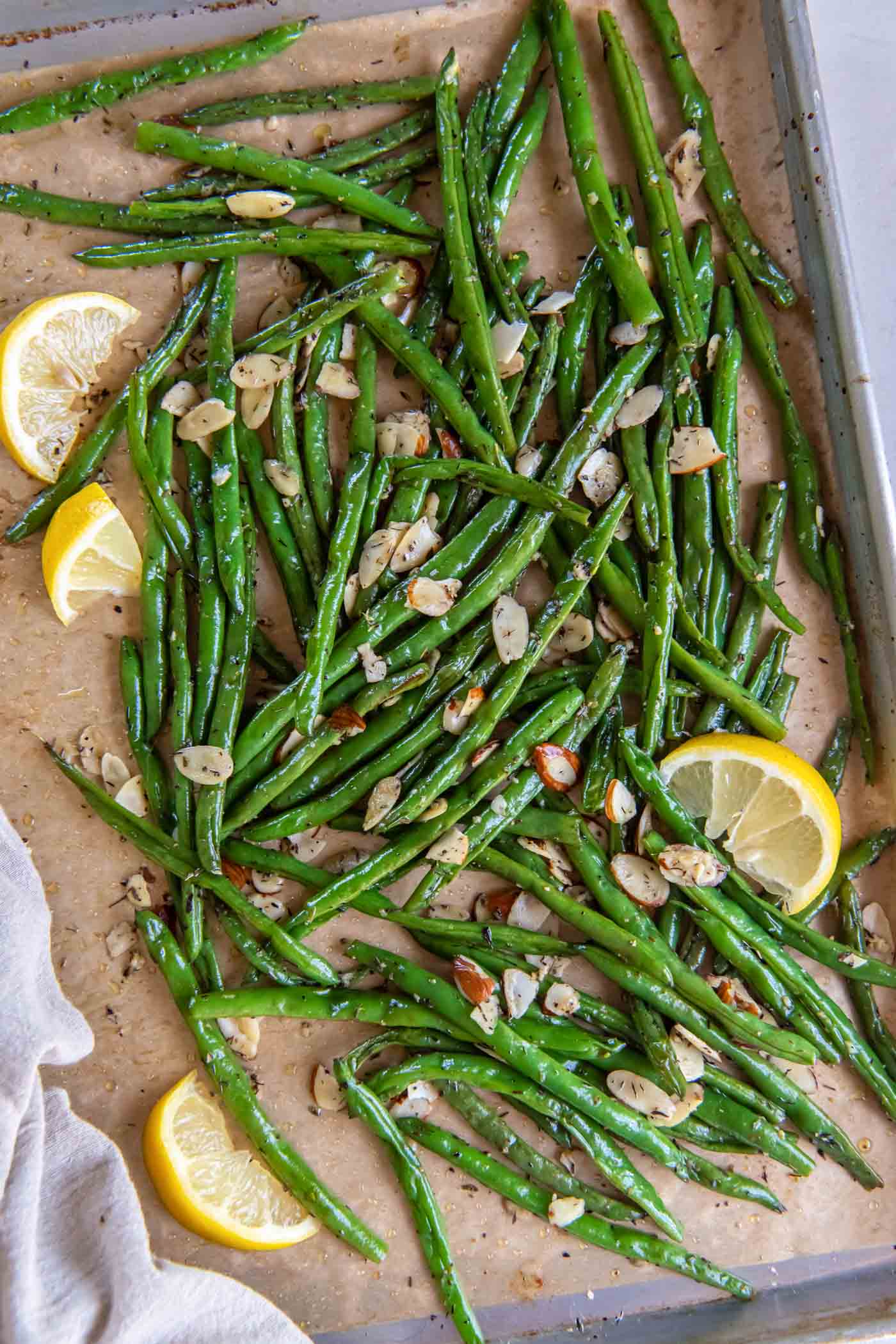 Roasted green beans with sliced almonds and lemon wedges on a baking sheet.