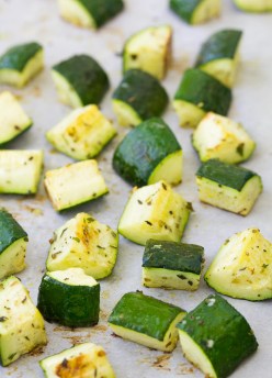 Cubes of roasted zucchini with seasonings on a baking sheet.