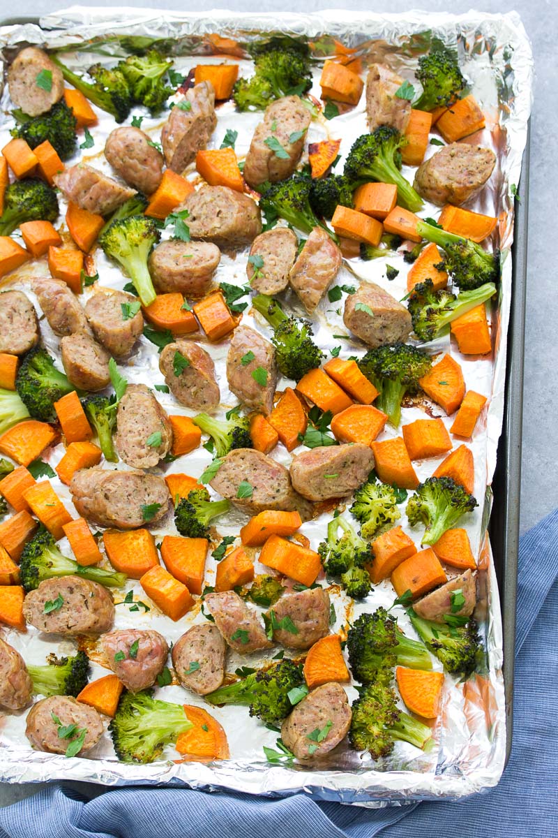 Cooked sausage, broccoli and sweet potatoes on a baking sheet.