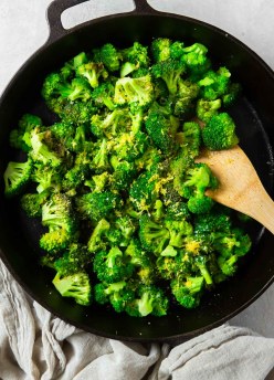 Sauteed broccoli in a cast iron skillet with wooden spatula.