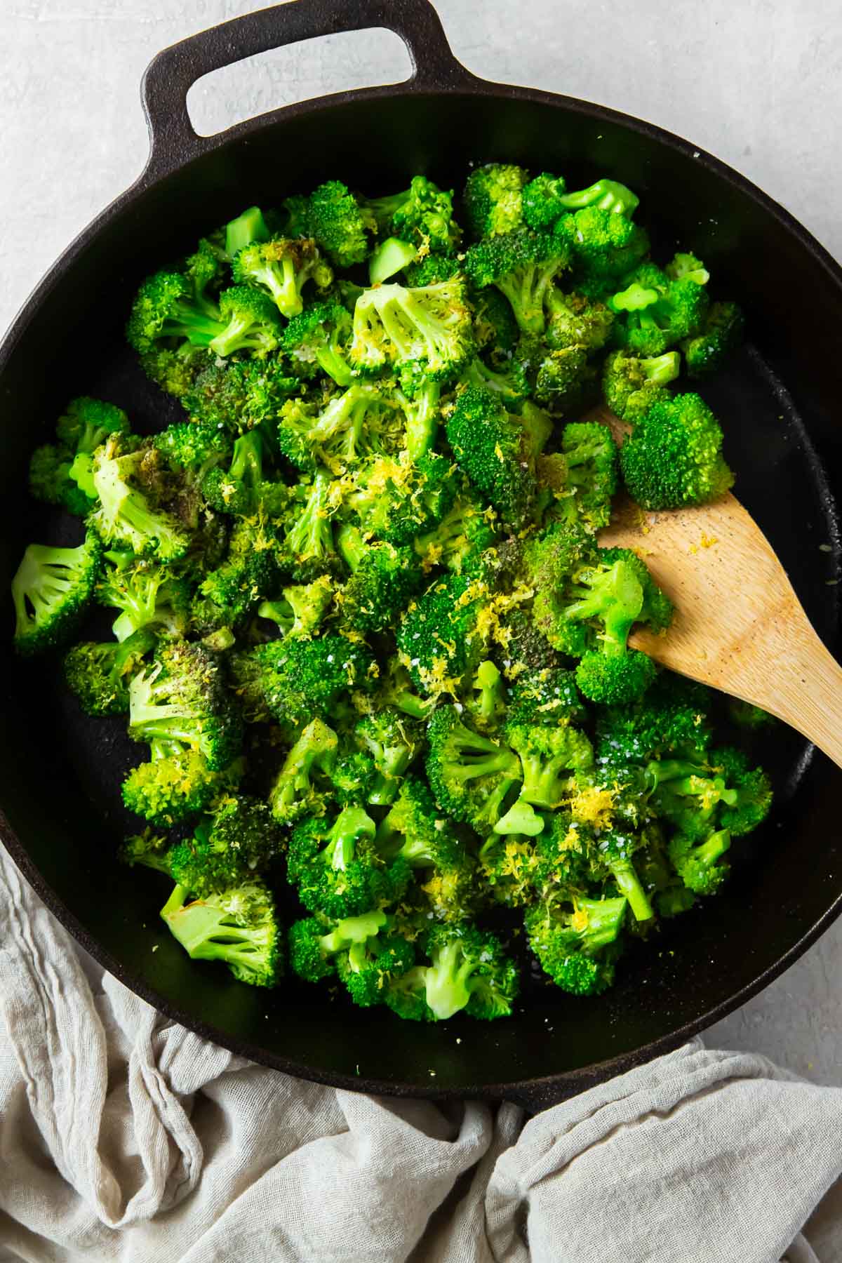Sauteed broccoli in a cast iron skillet with wooden spatula.