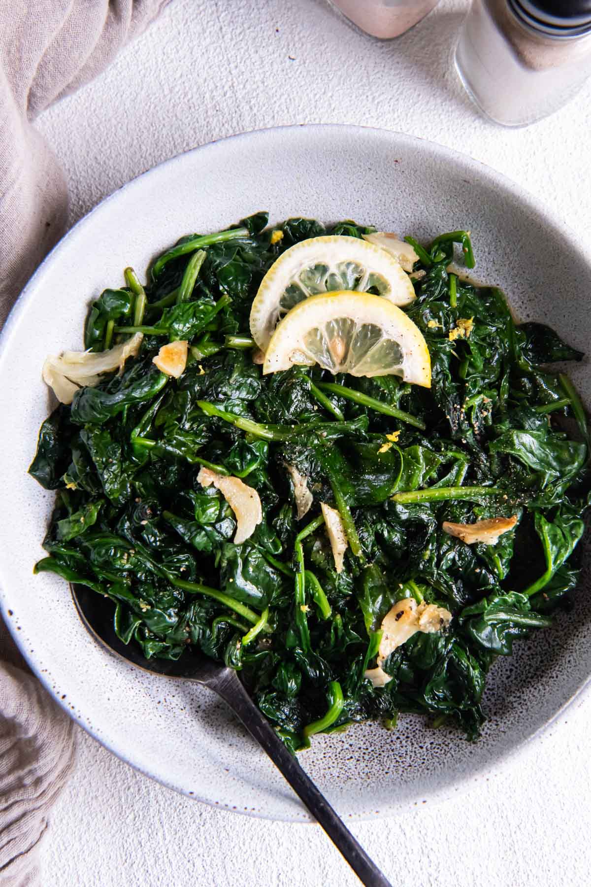 Sautéed spinach with garlic and lemon wedges in a serving bowl with a spoon.