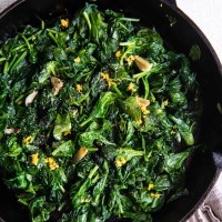 Sautéed spinach with smashed garlic cloves and lemon zest in a cast iron skillet.