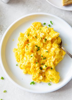 Scrambled eggs with chives served on a white plate with a fork.