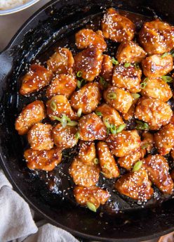 Sesame chicken in a cast iron skillet with sesame seeds and green onions sprinkled on top.