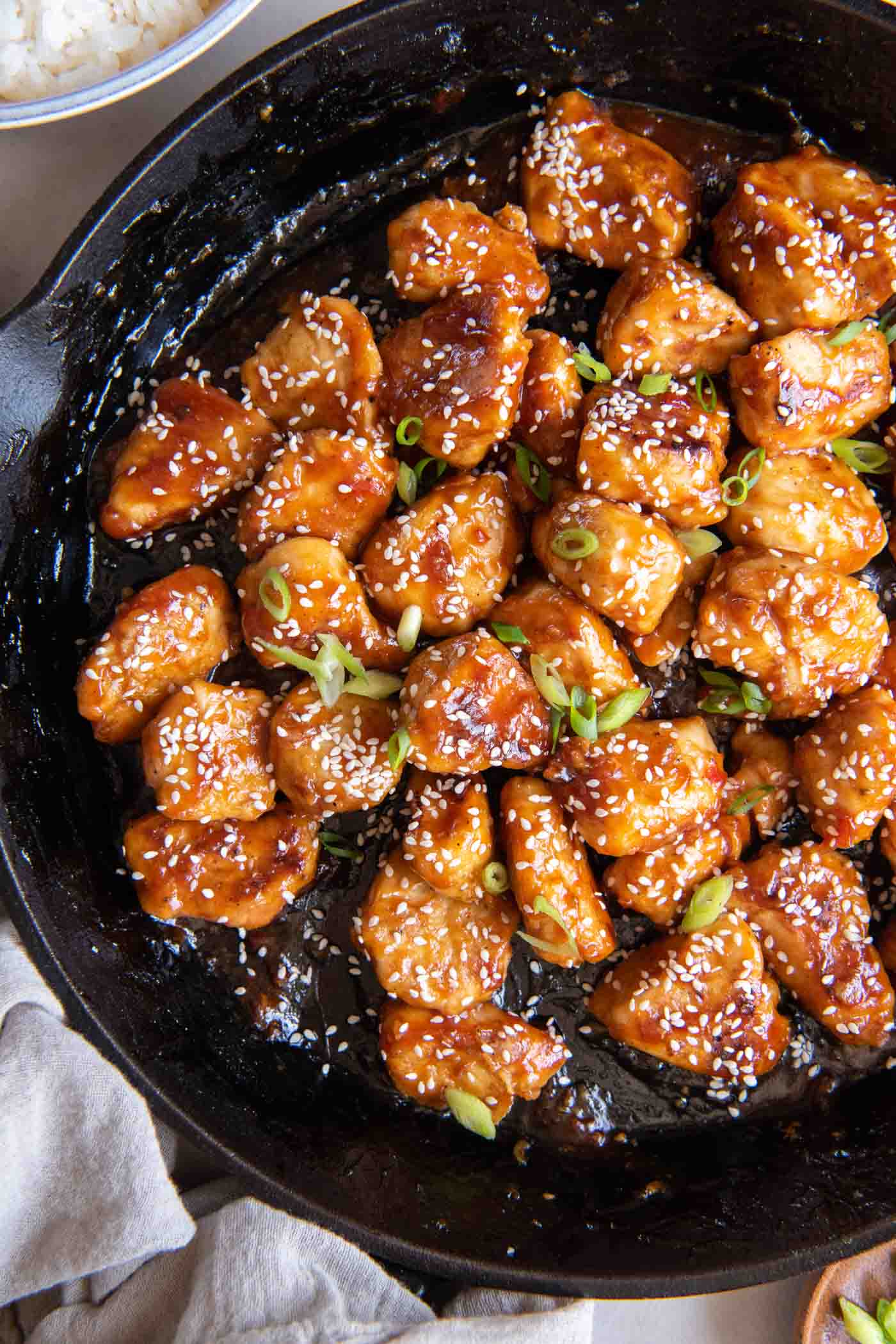 Sesame chicken in a cast iron skillet with sesame seeds and green onions sprinkled on top.