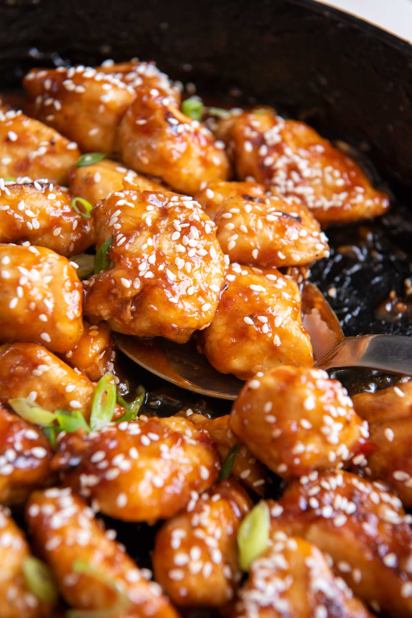 Close up of sesame chicken pieces on a spoon set in a skillet.