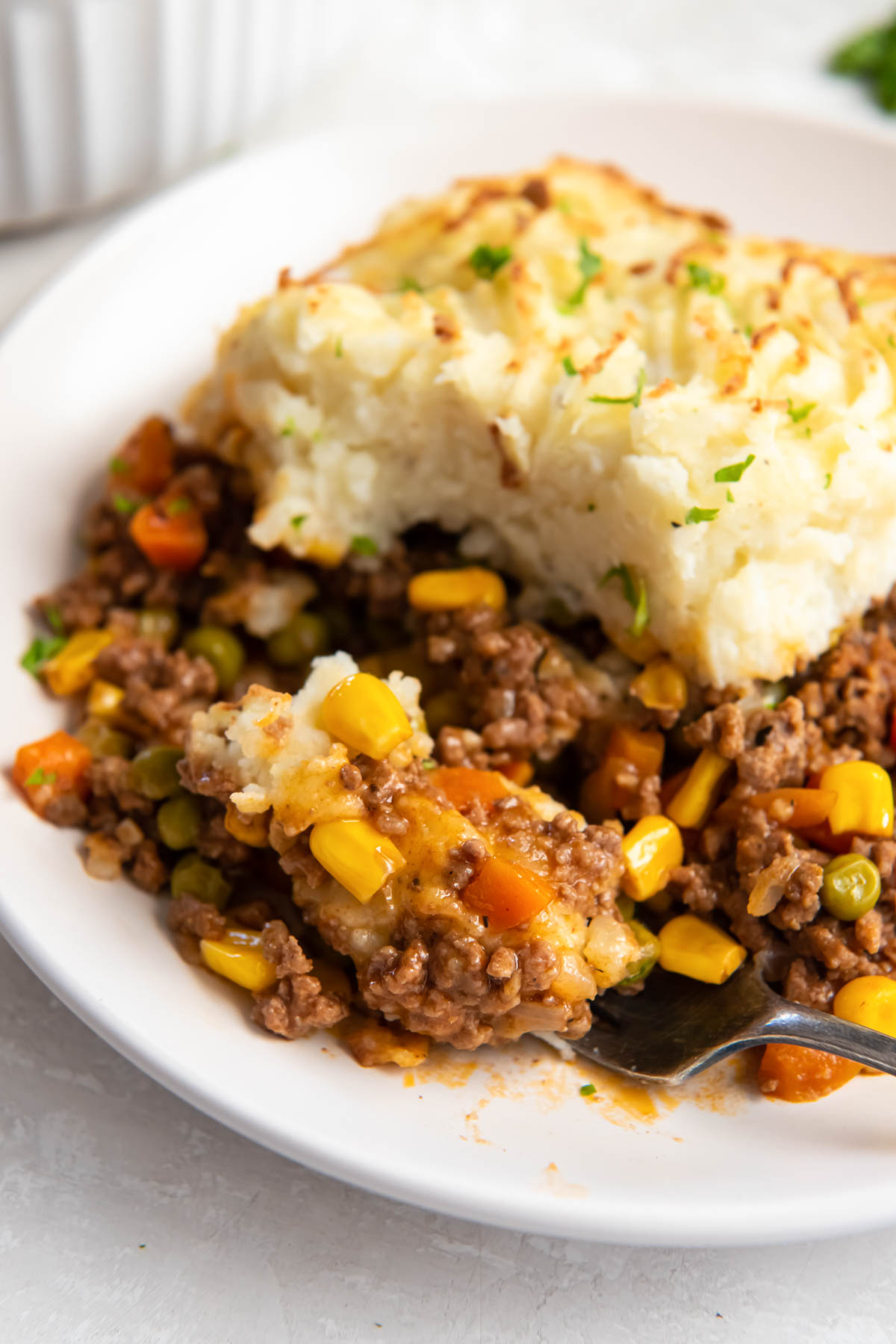 Close up of a serving of shepherd's pie on a plate with bite on a fork.