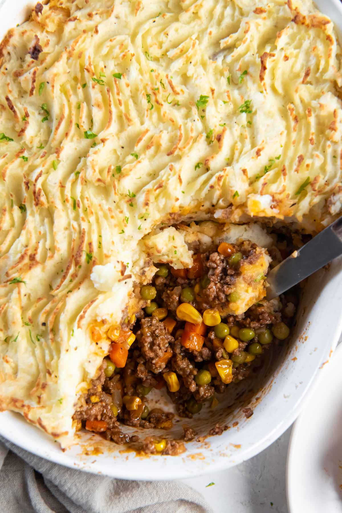 Baked shepherd's pie in dish with a serving spoon.