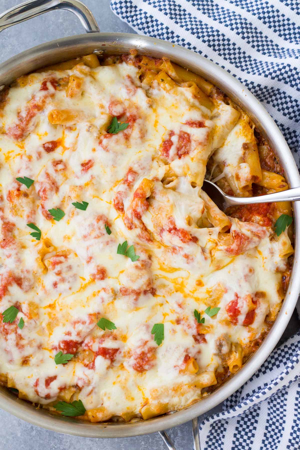 Baked ziti in a skillet with a serving spoon.