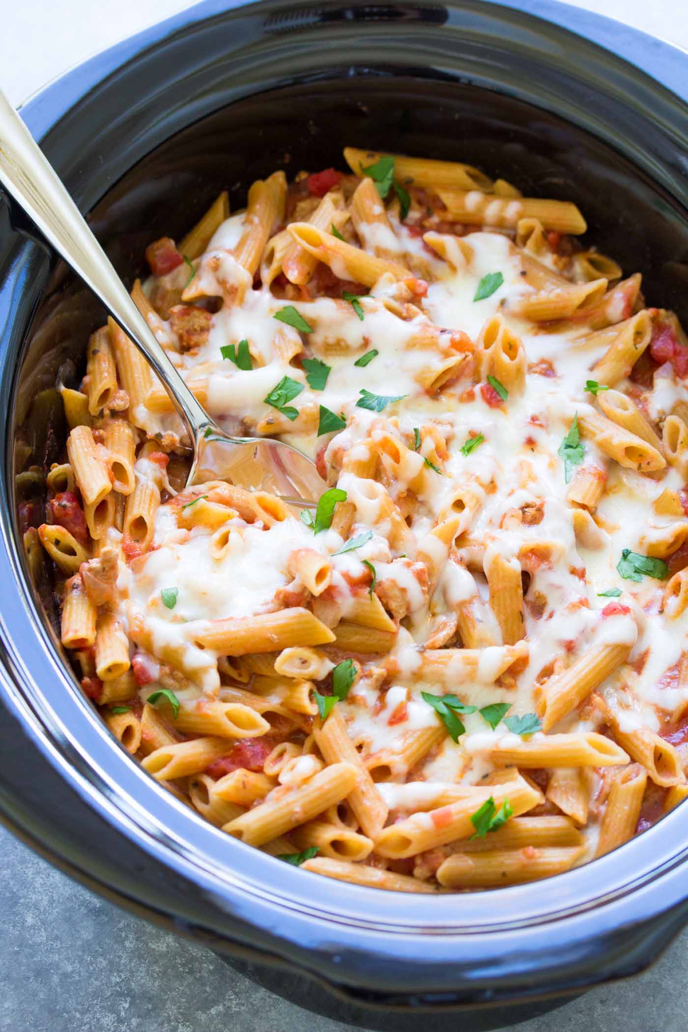 Slow cooker baked ziti in crockpot with serving spoon.