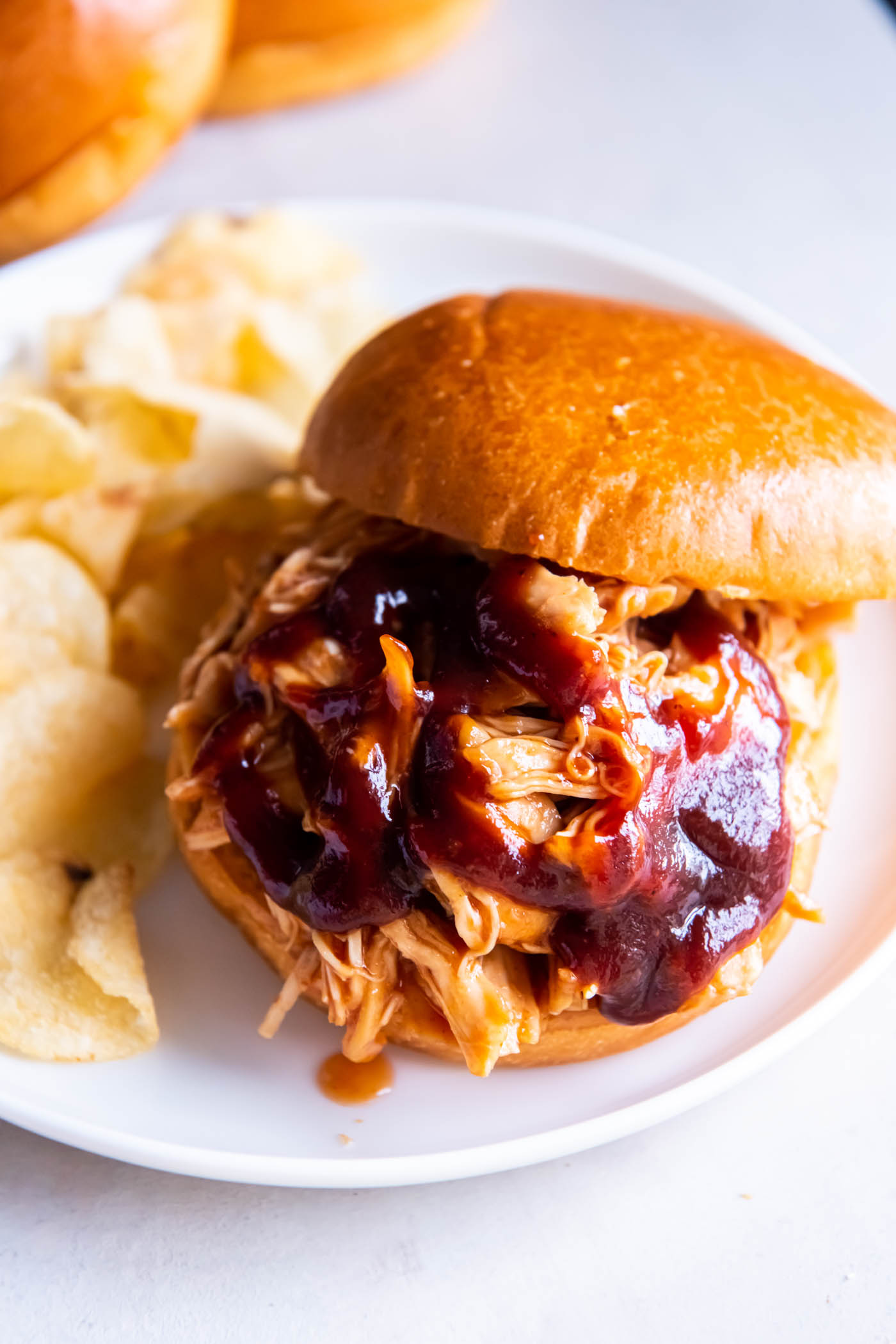 Shredded bbq chicken served on burger bun with bbq sauce.