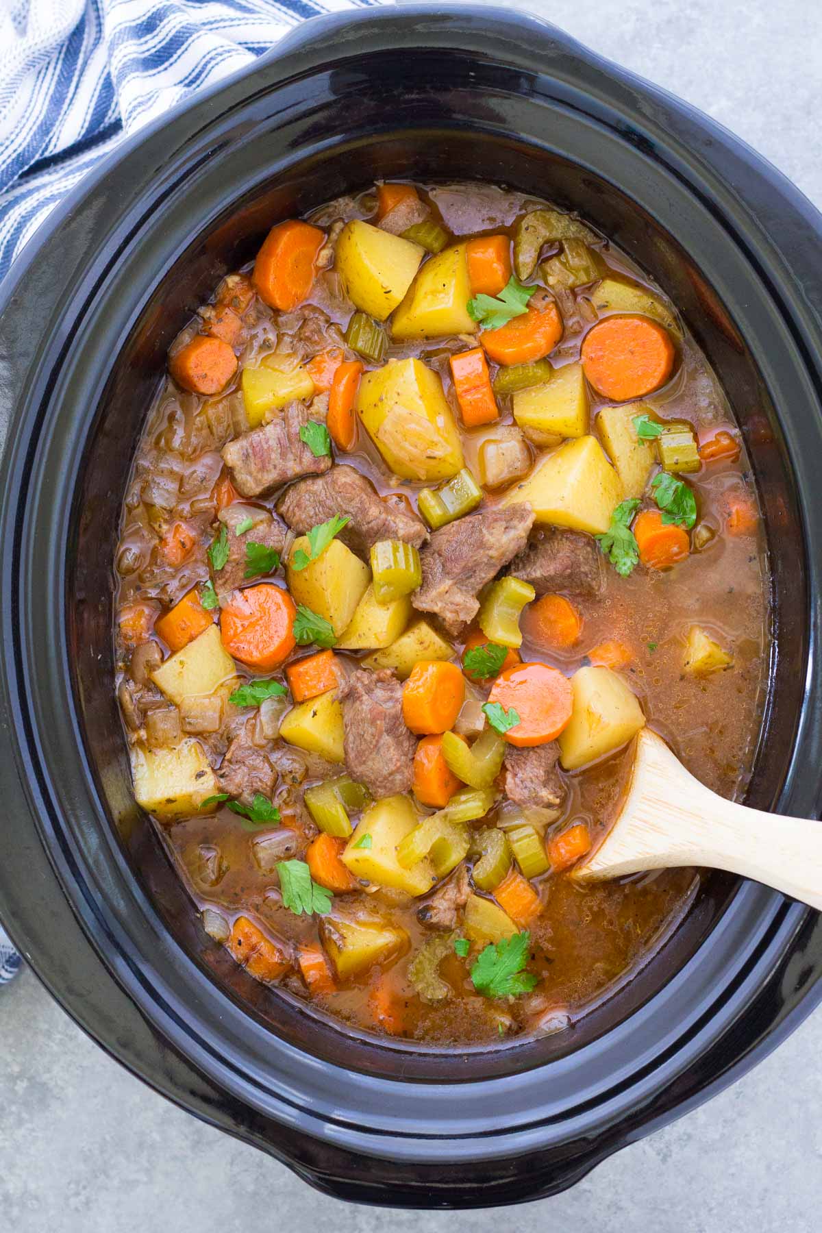 Beef stew in a slow cooker with a wooden spoon.