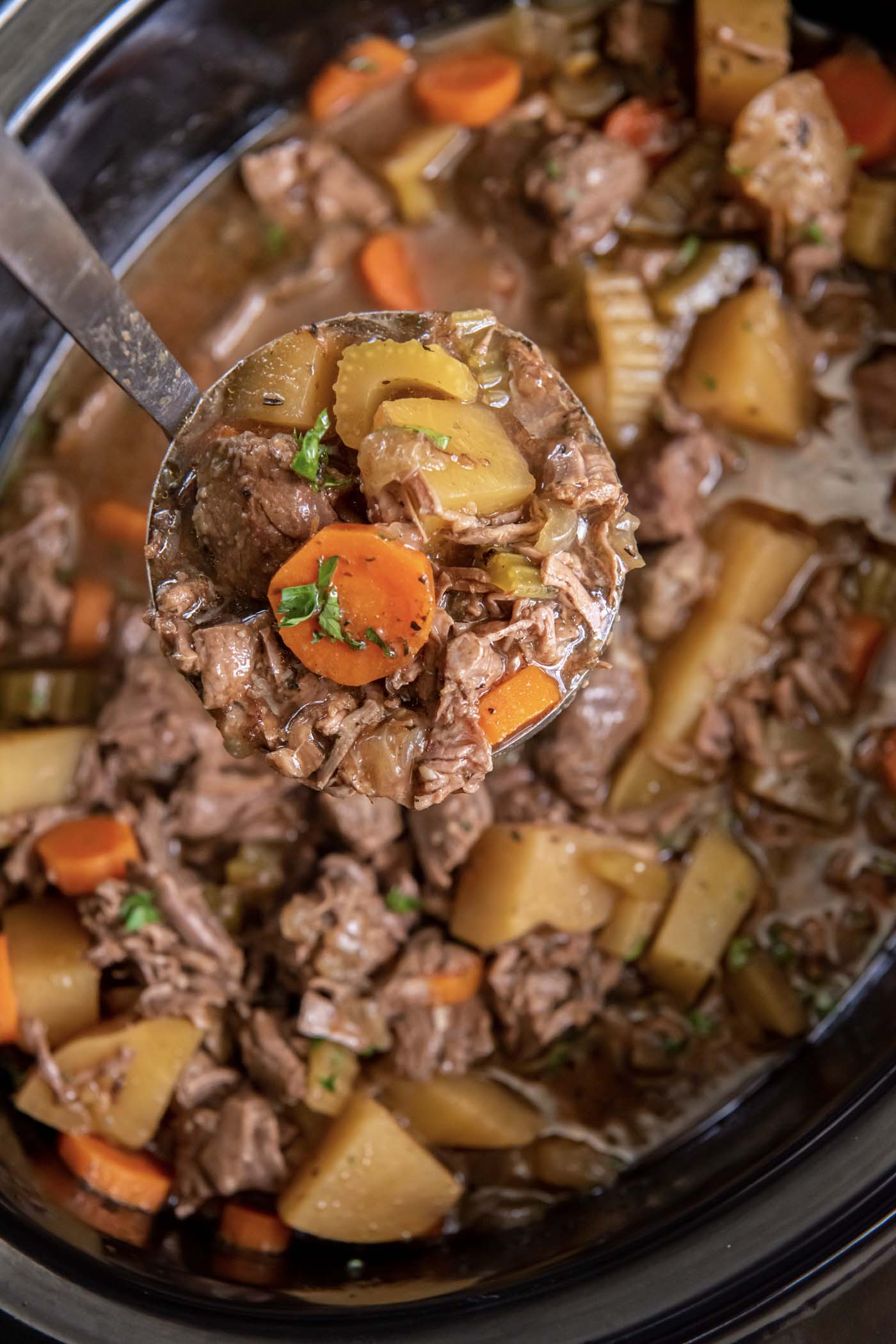Ladle of beef stew held over stew in crockpot.