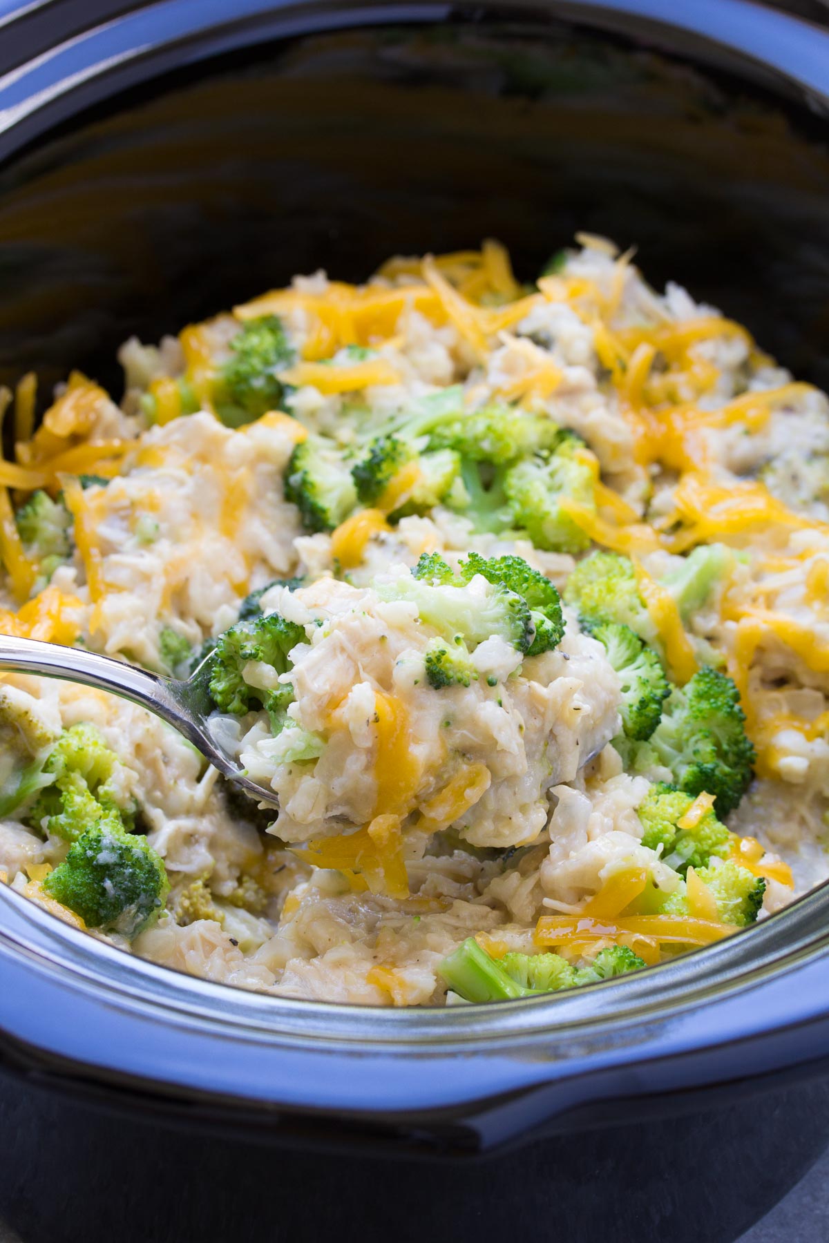 Chicken broccoli rice casserole in slow cooker with serving spoon.