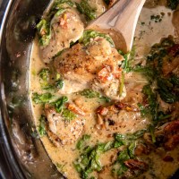 Tuscan chicken thighs in slow cooker with a wooden spoon.
