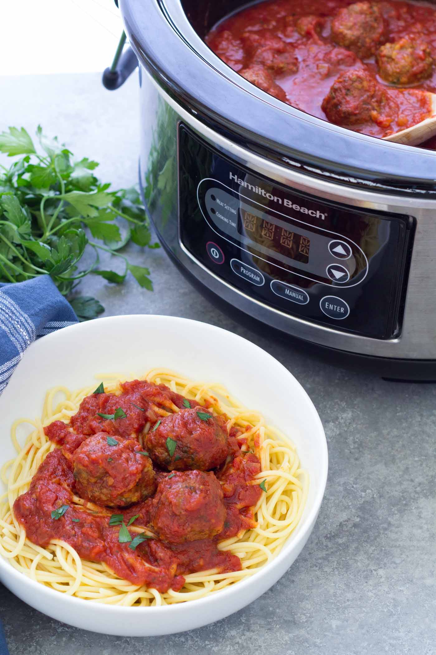 Crockpot meatballs served over spaghetti with slow cooker in the background.