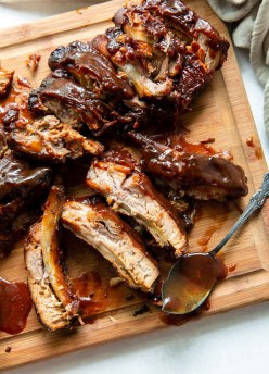 Slow cooker ribs with bbq sauce on a wood cutting board with bbq sauce spoon.