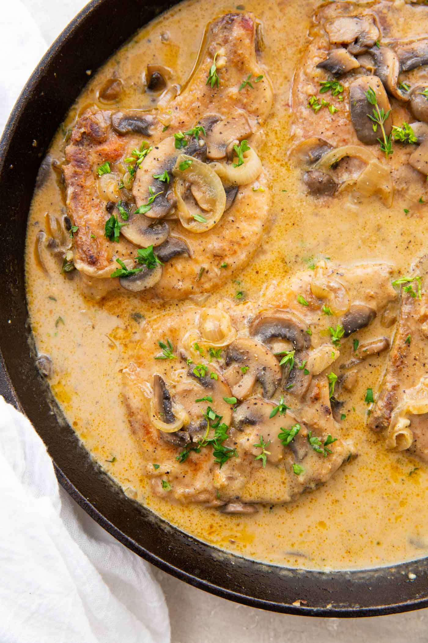 Smothered pork chops in creamy sauce in cast iron skillet.