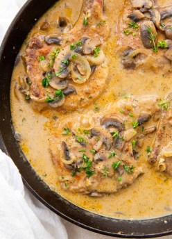 Smothered pork chops with creamy mushroom gravy in cast iron skillet.