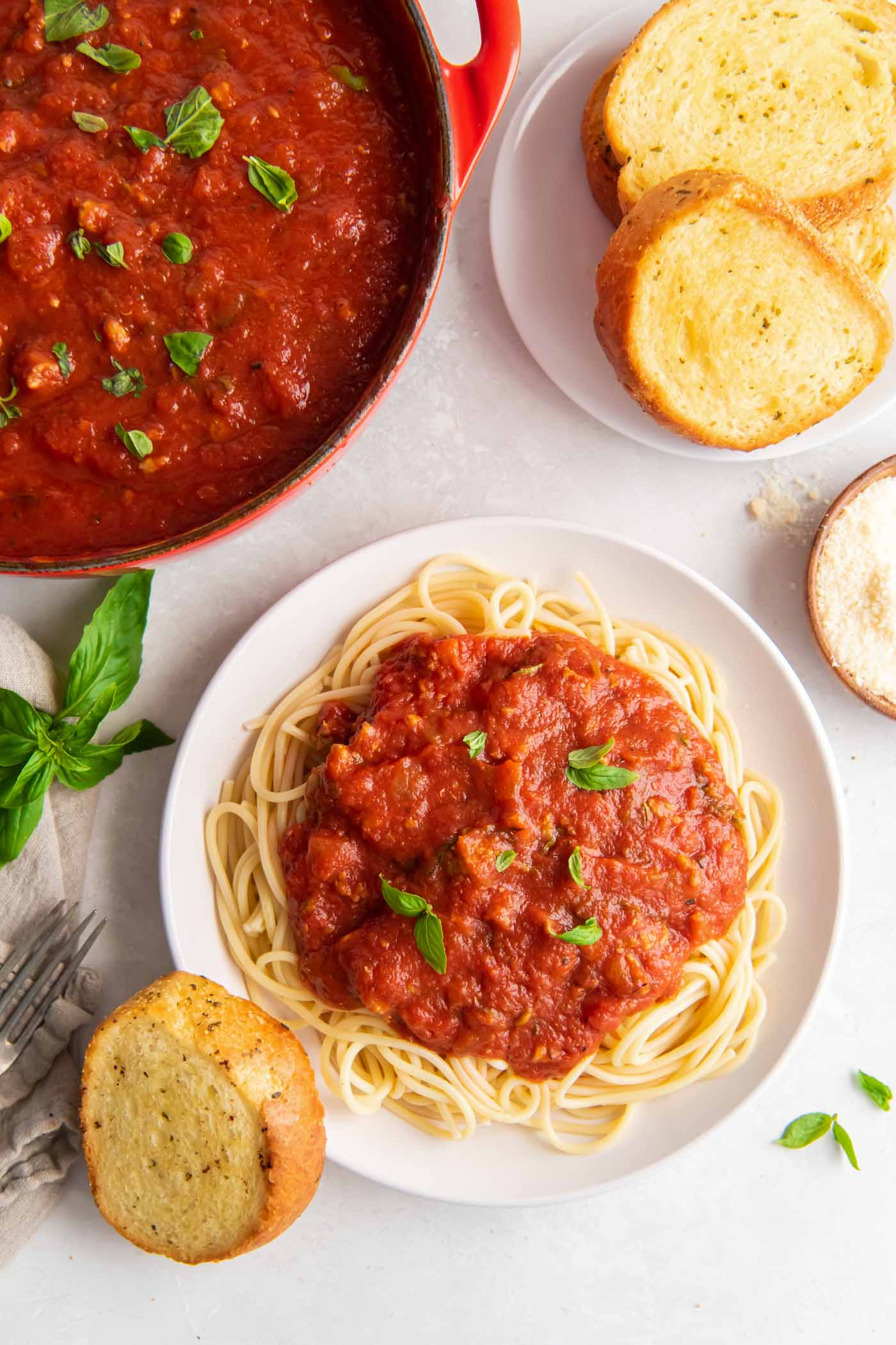 Plate of spaghetti with sauce served with garlic bread, with pot of sauce in background.