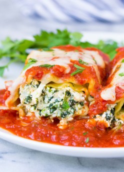 two cheesy spinach lasagna roll ups on a plate with marinara sauce