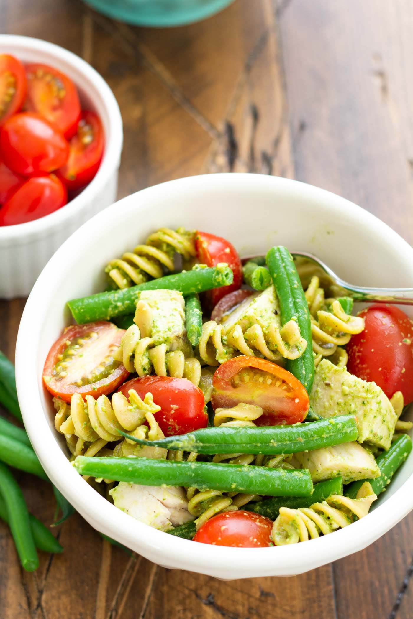Chicken pesto pasta with green beans and tomatoes in a small bowl.