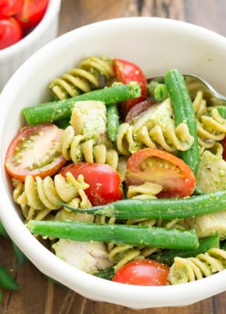 closeup of pesto pasta with chicken, tomatoes in a bowl with a fork