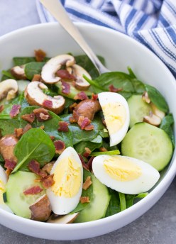 Spinach salad with bacon and eggs in a bowl.