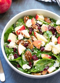 Spinach salad with apple, pecans and quinoa in a white bowl.
