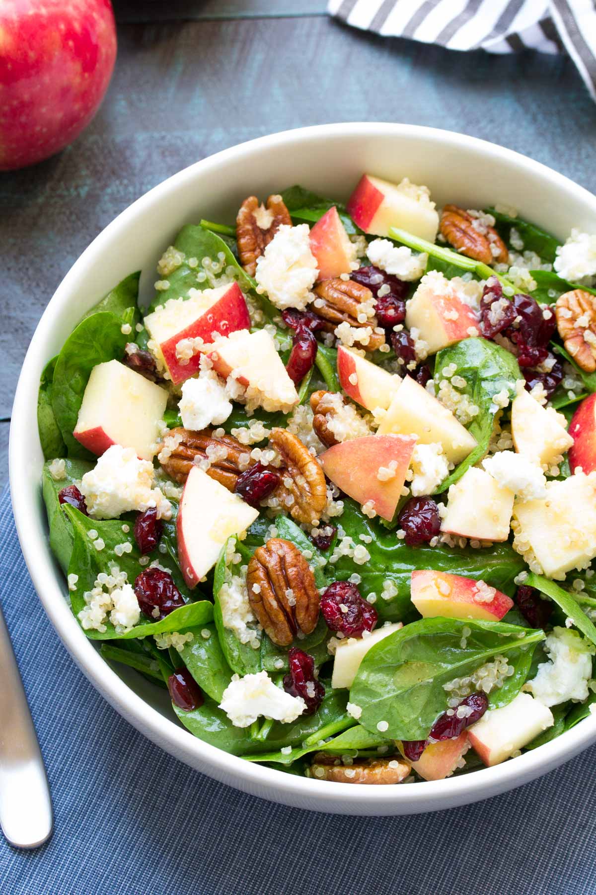 Spinach salad with apple, pecans and quinoa in a white bowl.