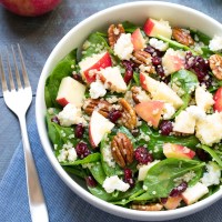 Spinach salad with apple and pecans in a white bowl.
