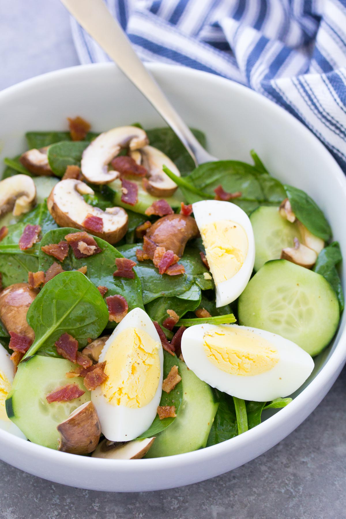 Spinach salad with bacon and hard boiled eggs in white bowl.