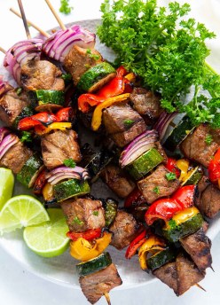 steak and vegetable kabobs stacked on a plate with lime and parsley
