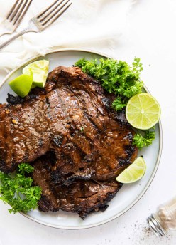 two grilled ribeye steaks on a plate with parsley and lime garnish