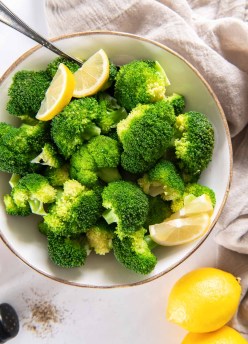 Steamed broccoli with lemon wedges in a serving bowl.