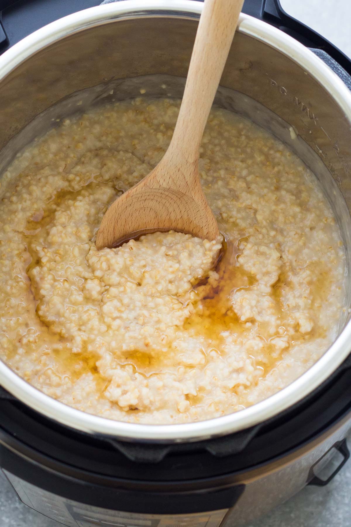 Cooked steel cut oats in instant pot with maple syrup drizzle and a wooden spoon.
